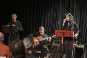 Tre artisti che si esibiscono in un concerto dal vivo, uno con clarinetto, uno con chitarra e una cantante.
